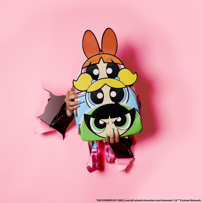 Two hands punching through a pink paper background holding the Powerpuff Girls Triple Pocket Backpack, featuring Blossom, Bubbles, and Buttercup on each pocket.